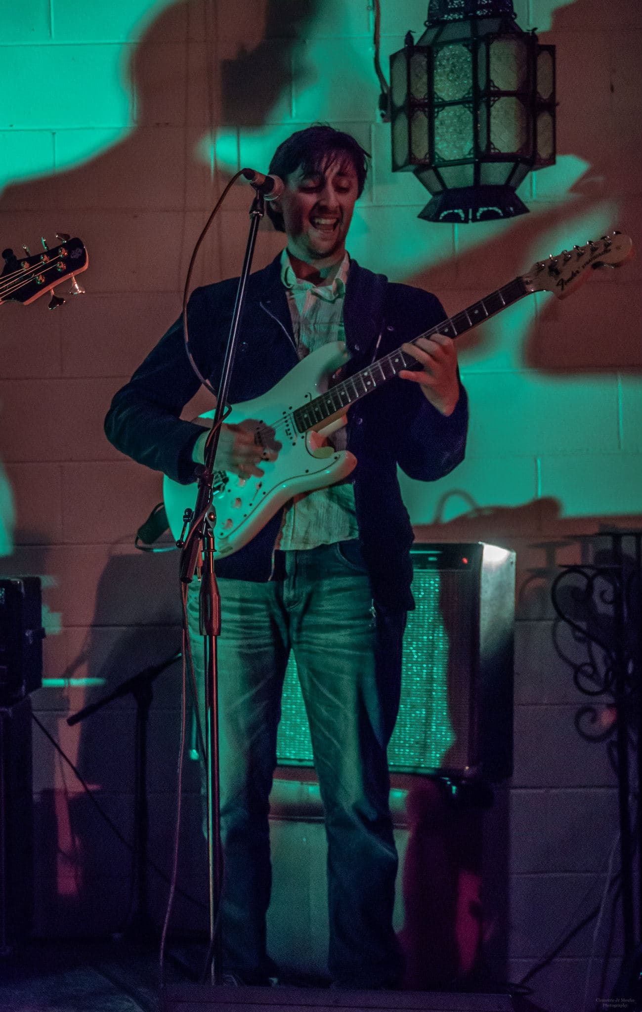 Ben stands at the mic playing a white electric guitar in front of an amp under green lighting.