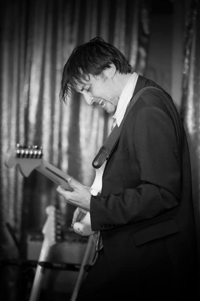 Ben leans over his guitar with hair falling forward, lost in playing, in a black-and-white live shot.