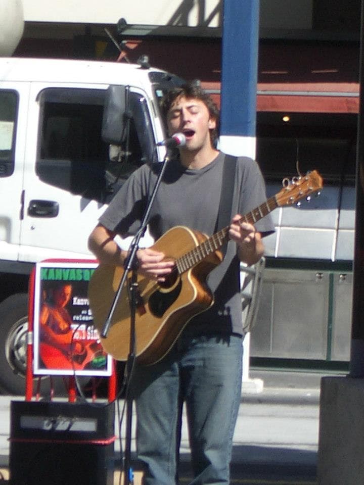 A younger Ben busks with an acoustic guitar beside a van and a Kanvas Grey single poster.