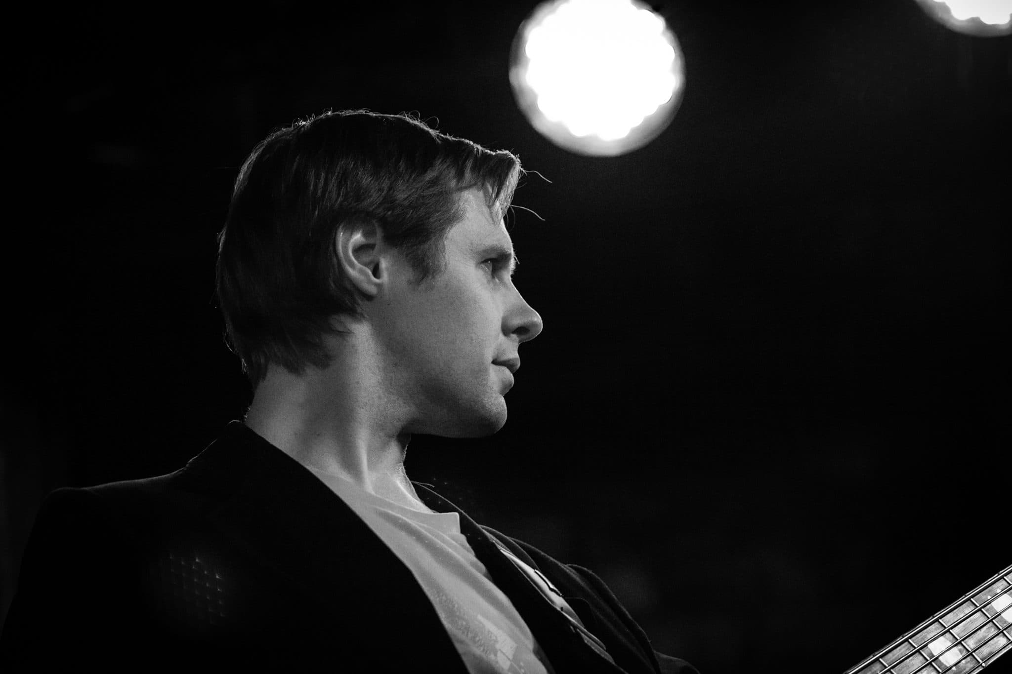 Moody black and white profile of Liam onstage with a bright spotlight glowing behind him.